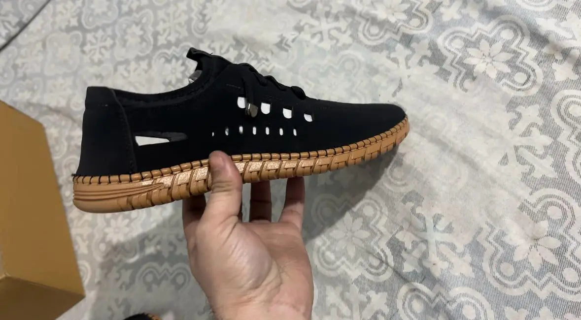 Black men's casual shoe with breathable design and brown sole held in hand