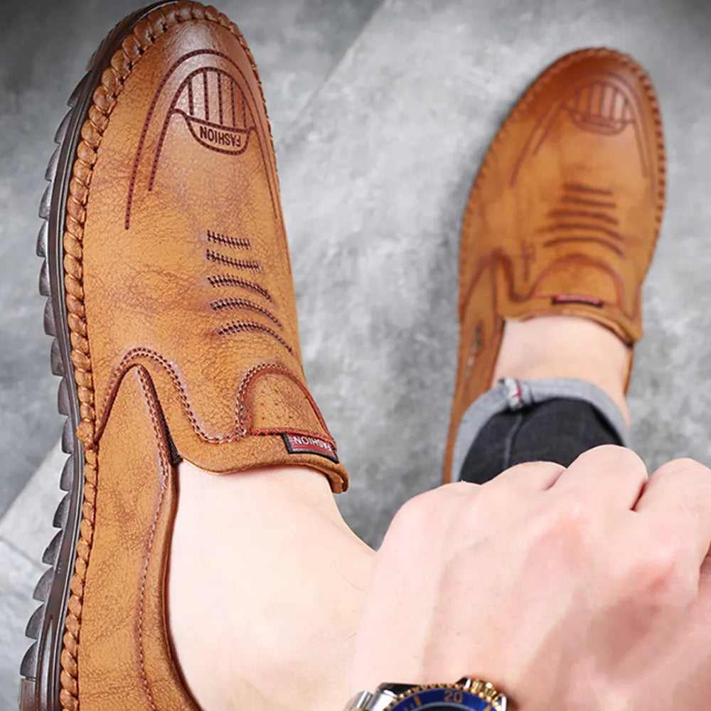 Brown soft leather casual shoes for men worn with black pants on a gray surface