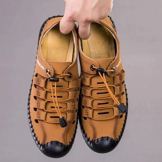 Hand holding tan men's casual shoes with black toe caps and adjustable laces trendsetting men's footwear